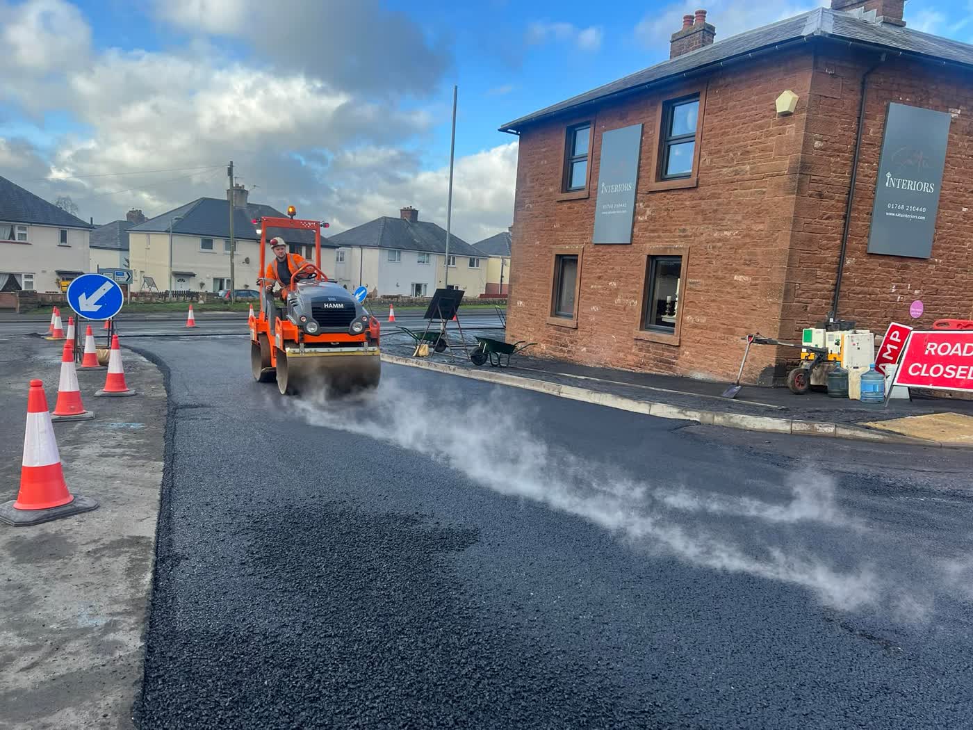 Dinsdale roller compacting fresh steaming tarmac on a village road in Cumbria